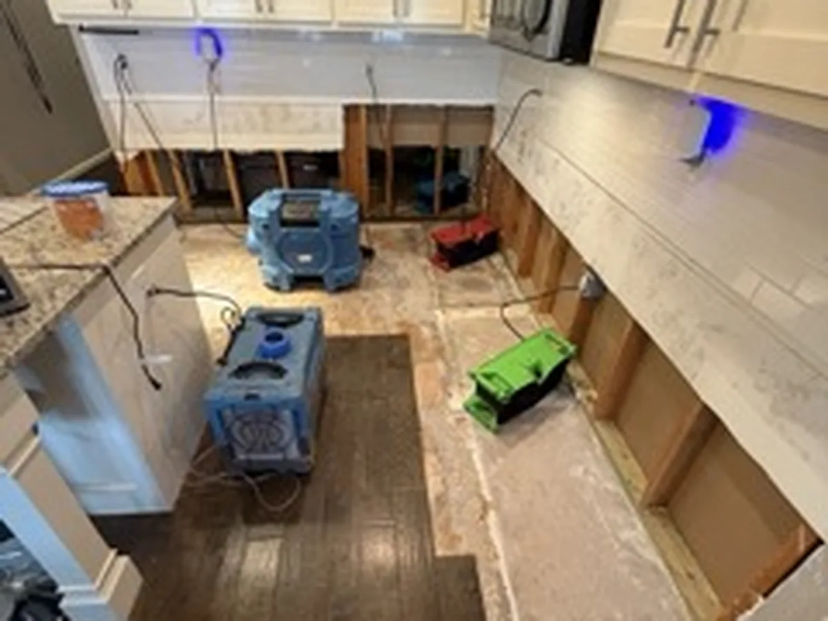 Air movers drying under flood-cut kitchen cabinets and hardwood flooring after a water leak in an Oklahoma City home
