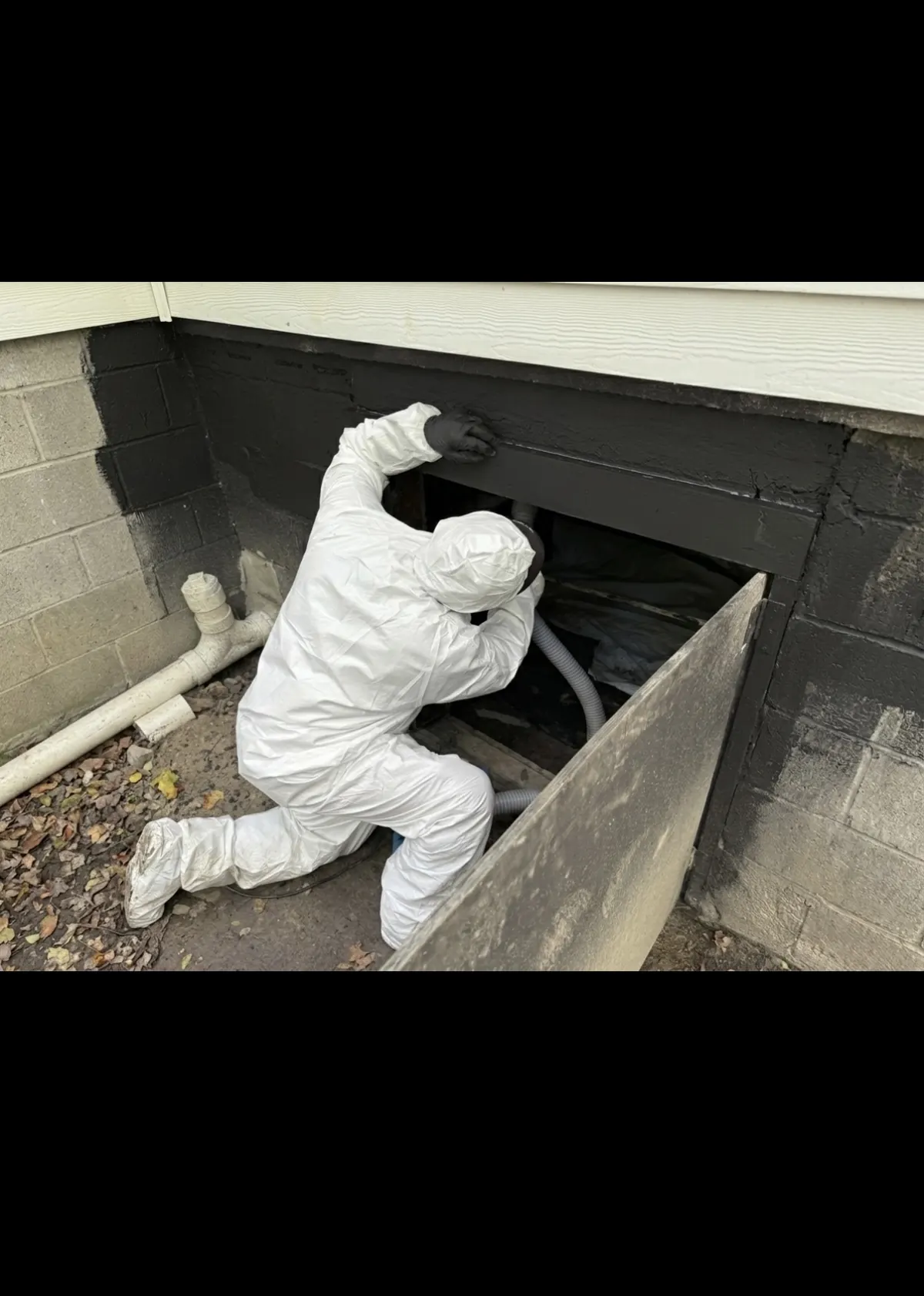 IICRC-certified technician in Tyvek suit entering a crawlspace access for mold remediation in Oklahoma