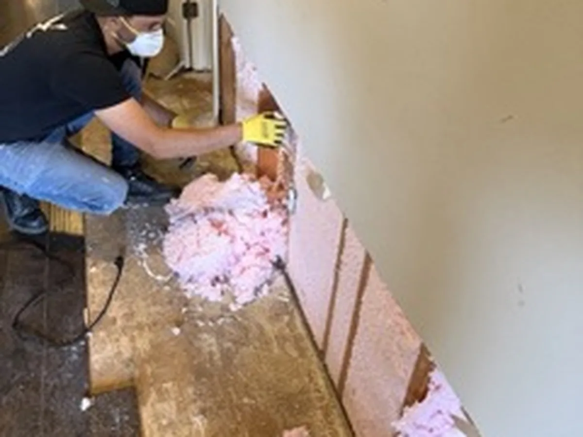 ASAP Pro technician in a respirator removing water-damaged drywall and wet insulation from a wall cavity